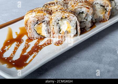 Sushi Imposta nigiri, Uramaki, California, Philadelphia, su un piatto bianco. Zenzero e wasabi nelle vicinanze. Salsa di soia in un recipiente bianco. Su uno sfondo grigio chiaro Foto Stock