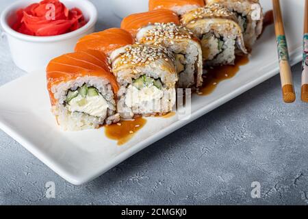 Sushi Imposta nigiri, Uramaki, California, Philadelphia, su un piatto bianco. Zenzero e wasabi nelle vicinanze. Salsa di soia in un recipiente bianco. Su uno sfondo grigio chiaro Foto Stock