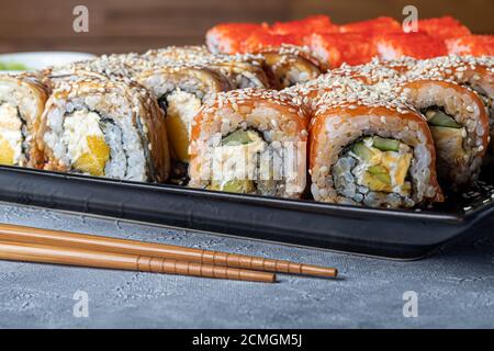 Sushi Imposta nigiri, Uramaki, California, Philadelphia, su un piatto bianco. Zenzero e wasabi nelle vicinanze. Salsa di soia in un recipiente bianco. Su uno sfondo grigio chiaro Foto Stock