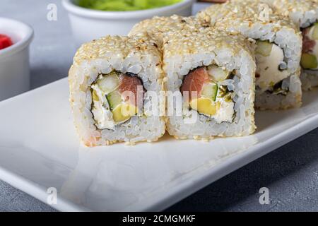 Sushi Imposta nigiri, Uramaki, California, Philadelphia, su un piatto bianco. Zenzero e wasabi nelle vicinanze. Salsa di soia in un recipiente bianco. Su uno sfondo grigio chiaro Foto Stock