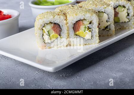 Sushi Imposta nigiri, Uramaki, California, Philadelphia, su un piatto bianco. Zenzero e wasabi nelle vicinanze. Salsa di soia in un recipiente bianco. Su uno sfondo grigio chiaro Foto Stock