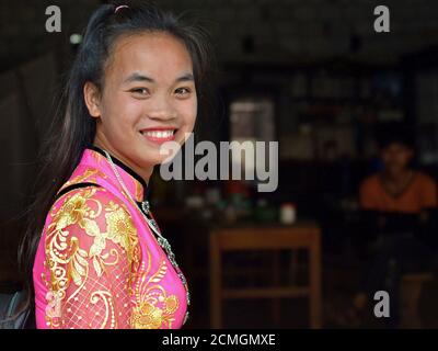 Bella giovane donna hmong hill-tribe vietnamita indossa un abito rosa e oro tradizionale in pizzo di seta e sorride per la macchina fotografica. Foto Stock