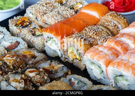 Sushi Imposta nigiri, Uramaki, California, Philadelphia, su un piatto bianco. Zenzero e wasabi nelle vicinanze. Salsa di soia in un recipiente bianco. Su uno sfondo grigio chiaro Foto Stock