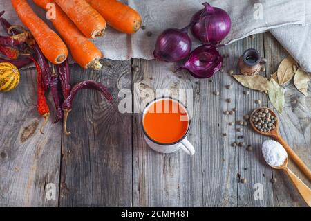 Fresco di succo di carota in una tazza di ferro sul grigio di una superficie di legno Foto Stock