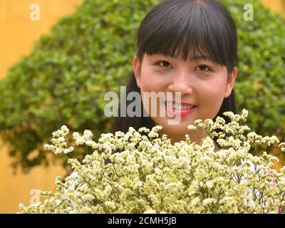 Bella giovane fiorista vietnamita mostra un bouquet floreale di fiori crema staticce e sorrisi per la macchina fotografica. Foto Stock