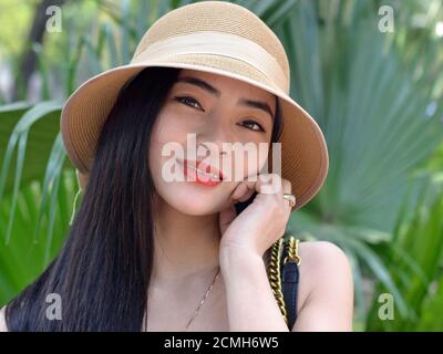 Bella donna del sud-est asiatico indossa un cappello da sole moderno e sorride per la macchina fotografica. Foto Stock