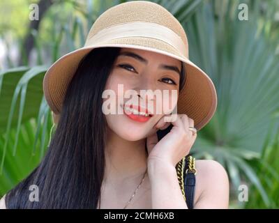 Bella donna del sud-est asiatico indossa un cappello da sole moderno e sorride per la macchina fotografica. Foto Stock