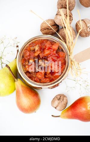 Confettura di pere con l'aggiunta di noci in un vaso di vetro su uno sfondo bianco primo piano. Foto Stock