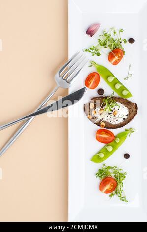 Insalata di giovani piselli verdi, pomodori e crostini con panna su un piatto bianco rettangolare su un pastello Foto Stock