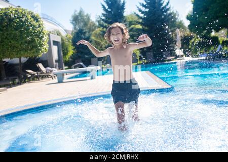 Ragazzo entusiasta che corre nella piscina all'aperto Foto Stock