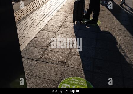 Uomo viaggiatore silhouette in piedi con bagagli in attesa per il treno. "Mantieni la distanza" è il testo della grafica di colore verde incollata sul pavimento Foto Stock