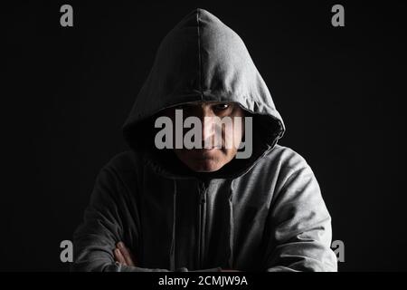 Un uomo ci dà uno sguardo sinistro che si nasconde nelle tenebre, con il volto parzialmente nascosto con una cappa grigia. Concetti di paura e pericolo. Scatto in studio. Foto Stock