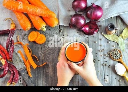 Mani femminili holding succo di carota in una tazza di ferro Foto Stock