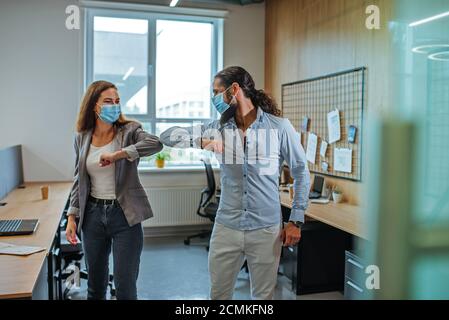 Gomito di saluto informale bump da uomini d'affari nelle maschere mediche in ufficio durante lo scoppio della pandemia globale COVID-19. Evitare la stretta di mano Foto Stock