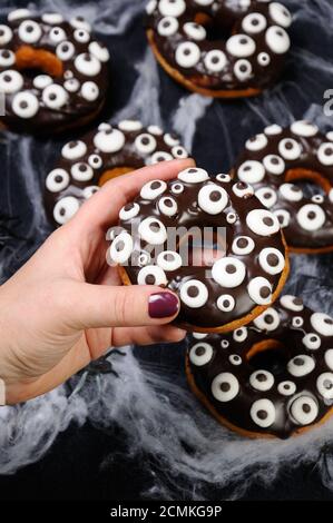 La mano tiene una ciambella con glassa di cioccolato decorato occhi d'oca Su Halloween Foto Stock