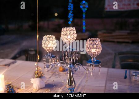 preparazione con lanterne, candele e luce e candelabra per cerimonia di compleanno di nozze su tovaglia bianca di notte. Foto di alta qualità Foto Stock