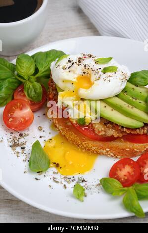 Uovo in camicia su una fetta tostata di baguette con pomodoro, prosciutto piccante e avocado, spezie spruzzate e Foto Stock