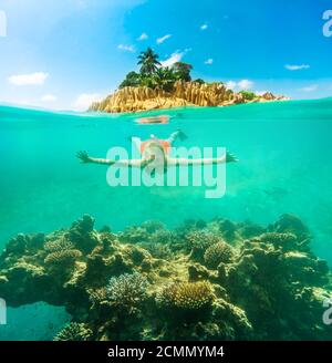 Vista divisa dell'apnea femminile sott'acqua e del paesaggio paradisiaco dell'isola della barriera corallina. Donna snorkeling esplorando il foca dell'Oceano Indiano, sotto e. Foto Stock