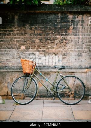 Una bicicletta tradizionale che si appoggia contro un muro di college dentro Cambridge, Regno Unito Foto Stock