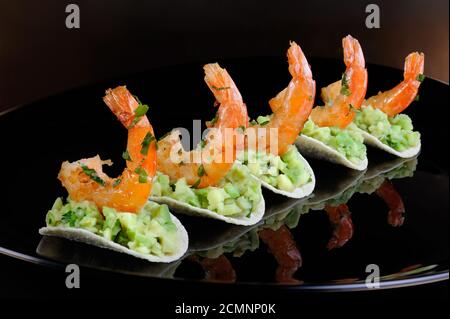 Uno snack leggero di patatine con riempimento di avocado e gamberi fritti aromatizzati con erbe aromatiche. Foto Stock