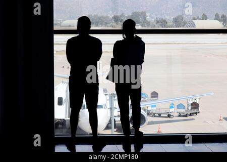 Coppia di passeggeri in aeroporto, sagome di un uomo e di una donna in maschere guardando l'aereo sulla asfalto attraverso il vetro Foto Stock
