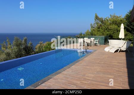 Piscina e area solarium sulla montagna con mare blu e alberi sullo sfondo. Villa di lusso sulla costa mediterranea, vacanza al mare Foto Stock