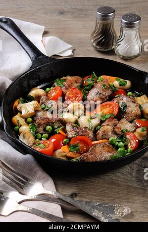 Fritti di fegato di pollo con verdura contorno di pomodori, carote, funghi piselli in padella Foto Stock