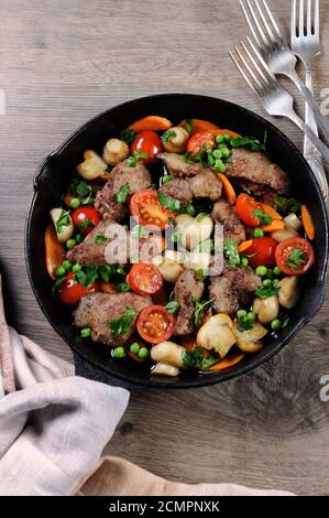 Fritti di fegato di pollo con verdura contorno di pomodori, carote, funghi piselli in padella Foto Stock
