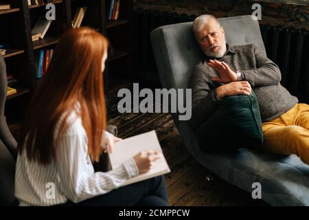 Psicologa professionale con capelli rossi giovane donna che consulta paziente uomo maturo Foto Stock