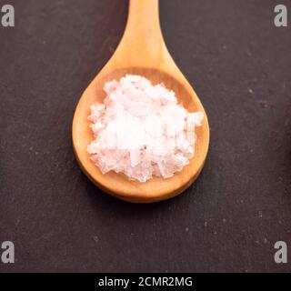 Il cucchiaio di legno con fiore di sale in scaglie su una piastra di ardesia Foto Stock