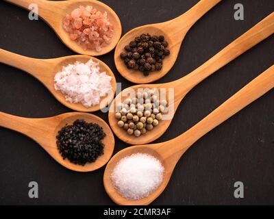 Cucchiai di legno con sale dell'himalaya, sale nero delle hawaii, sale comune, scaglie di sale e pepe in grani su un Foto Stock