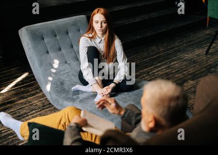 Frustrata giovane donna con capelli rossi in abbigliamento casual sta avendo sessione di terapia con psicologo. Foto Stock