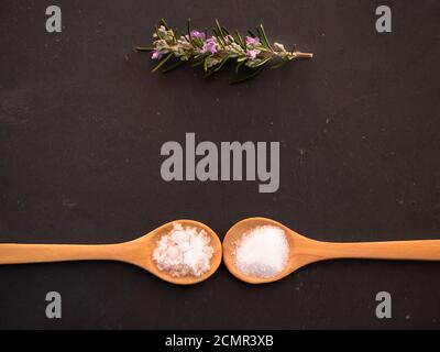 Cucchiai di legno con il comune sale marino e fiore di sale in scaglie su una piastra di ardesia Foto Stock