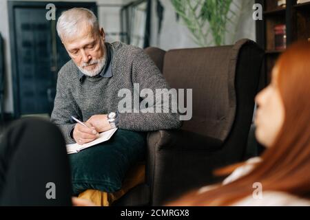 Psychologist dell'uomo maturo bearded con i capelli grigi sta sostenendo e consolando il paziente depresso Foto Stock