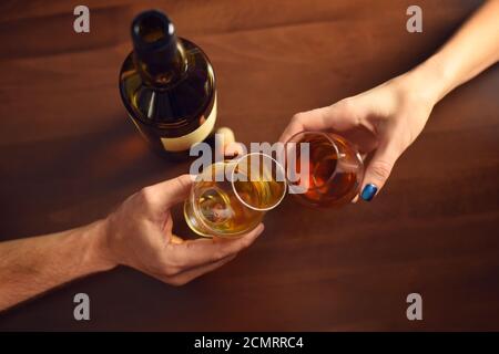 Una coppia fa un toast con due bicchieri di whisky su tavolo di legno, vista dall'alto Foto Stock
