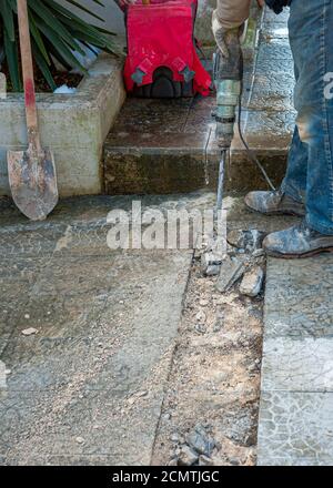 Il lavoratore di costruzione sta perforando il pavimento. I tecnici edili utilizzano scalpelli a martello elettrico per distruggere il terreno. Foto Stock