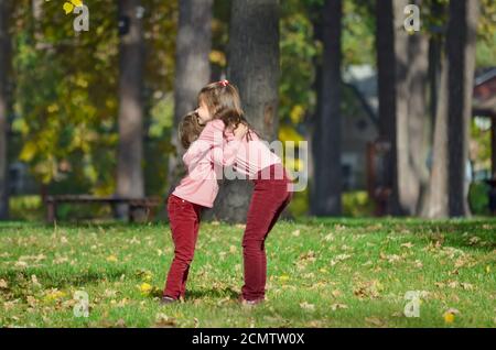 Due piccole sorelle in abiti identici si abbracciano durante una passeggiata nel parco in una calda giornata autunnale. Il concetto di una felice infanzia spensierata. Foto Stock