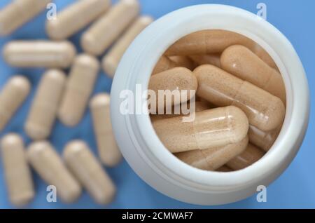 Flacone medicinale bianco con pillole su sfondo azzurro sfocato con capsule sparse, primo piano. Concetto di assistenza sanitaria. Foto Stock
