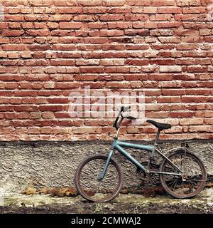 Vecchio arrugginito bicicletta vintage appoggiata contro un muro di mattoni Foto Stock
