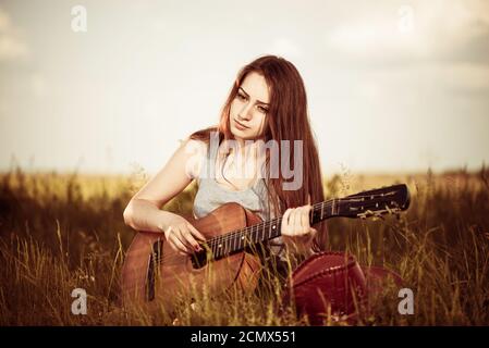 giovane donna in cappello con chitarra acustica al prato primaverile Foto Stock