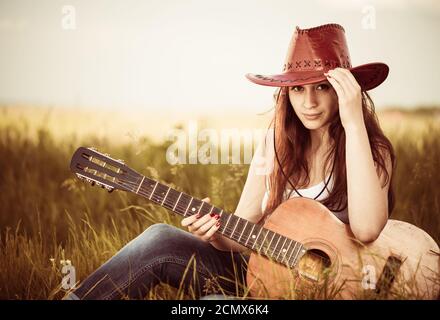 giovane donna in cappello con chitarra acustica al prato primaverile Foto Stock