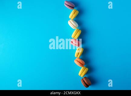 i macaron rotondi e multicolore al forno con panna si trovano in una linea su sfondo blu Foto Stock