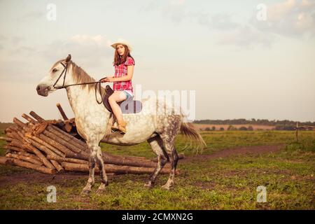 Giovane donna in cappello in estate fattoria tramonto cavalcare bianco cavallo Foto Stock