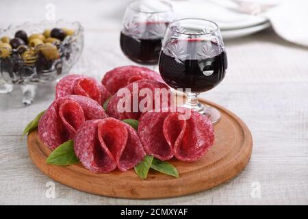 spuntino leggero da salame ripiegato a forma di fiore con un bicchiere di sherry su un piatto di legno. Cl Foto Stock