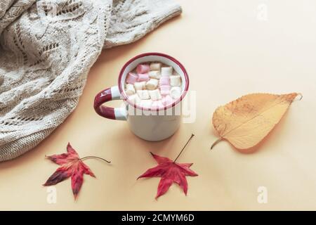 Una tazza di cacao con marshmallow, maglia maglione e foglie autunnali su sfondo giallo, concetto di caduta. Vista dall'alto. Foto Stock