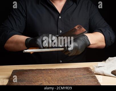 chef in una camicia nera e guanti in lattice nero affilare un coltello da cucina Foto Stock