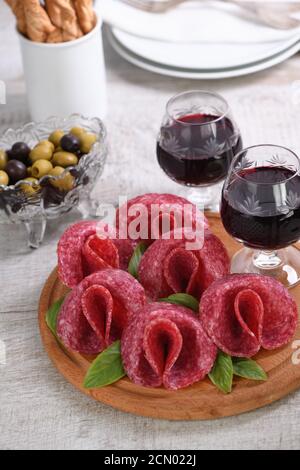 Pasto leggero snack dal salame piegato nella forma di un fiore con un bicchiere di sherry su un piatto di legno. Foto Stock