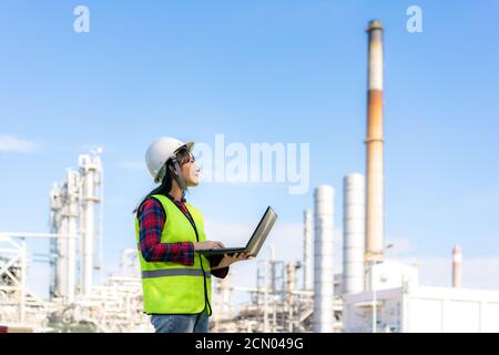 Donna asiatica ingegnere petrolchimico che lavora di notte con un computer portatile all'interno di petrolio e gas raffineria stabilimento di industria di notte per la sicurezza ispettore quali Foto Stock