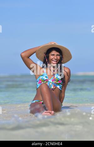 Donna ispanica che si siede su una spiaggia con un bel bikini E cappello di paglia guardare camera.in Los Roques Venezuela Foto Stock