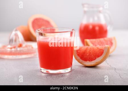 Un bicchiere di succo di pompelmo appena fatto e fette di frutta fresca su uno sfondo di cemento chiaro. H Foto Stock